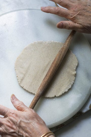 Rolling out a jowar roti on a rolling board with a pin.
