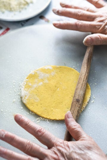 Two hands rolling out a roti with a wooden rolling pin.