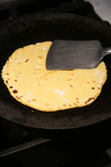 Spatula pressing down on a roti being cooked.