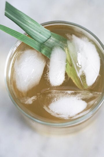 Iced lemongrass tea in a cup with two stalks of lemongrass, top down view of glass.