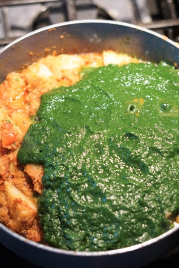 Spinach puree added to saag aloo in a pan.