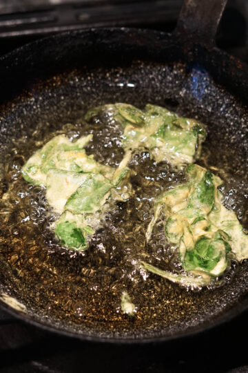 Spinach pakora frying in oil.