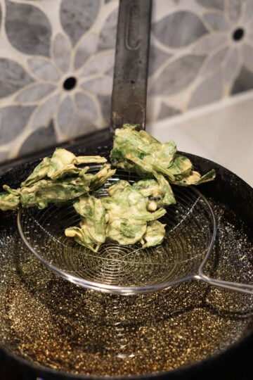 Fried spinach pakora being taken out of oil.