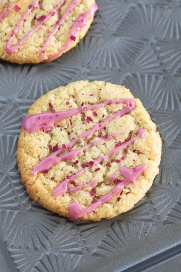 Eggless coconut cookies with a rose icing drizzled on top.