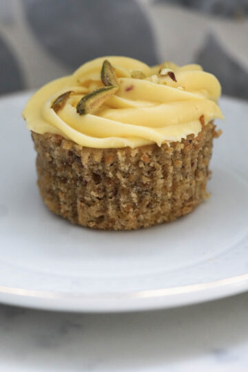 Frosted kesar pista cupcake on a white plate.