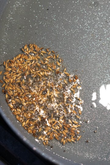 Cumin seeds sizzling in oil in a pan.