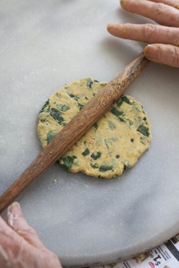 Rolling out a thepla with a wooden rolling pin.