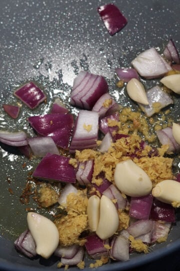 Red onions, ginger paste, and garlic cloves added to pan.