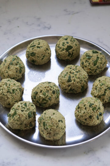 11 dough balls of methi dhebra on a steel plate.