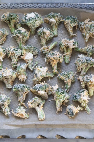 Coated broccoli pieces on a parchment paper.