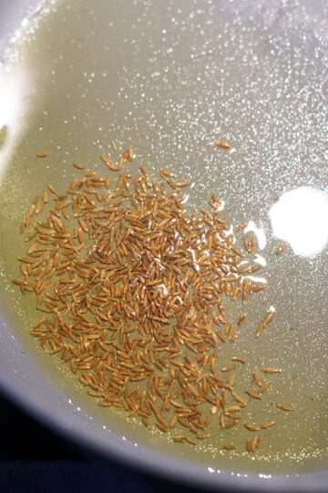 Cumin seeds cooking in olive oil in a pan.