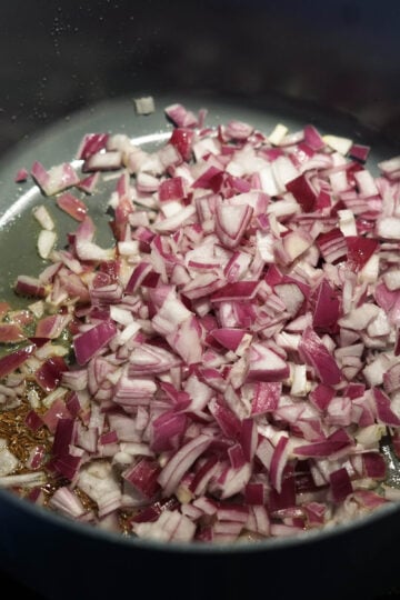Red onions added to cumin seeds and olive oil in a pan.
