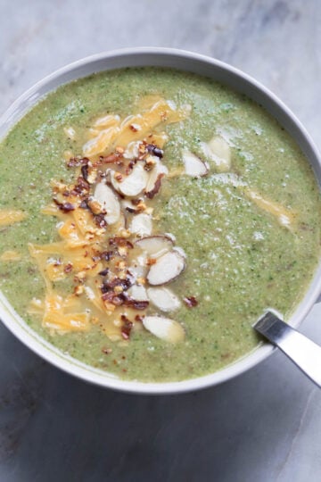 Almond broccoli soup garnished with cheddar cheese, red chili flakes, and chopped almonds in a bowl.