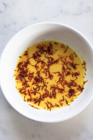 Saffron blooming in milk in a small white bowl.