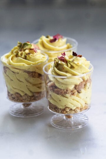 Eggless thandai cheesecake mousse cups garnished with rose petals and pistachios.